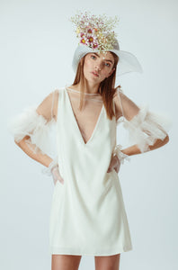 Model wears ivory mini dress with flower hat on her head