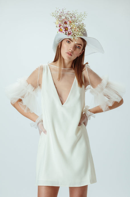 Model wears ivory mini dress with flower hat on her head